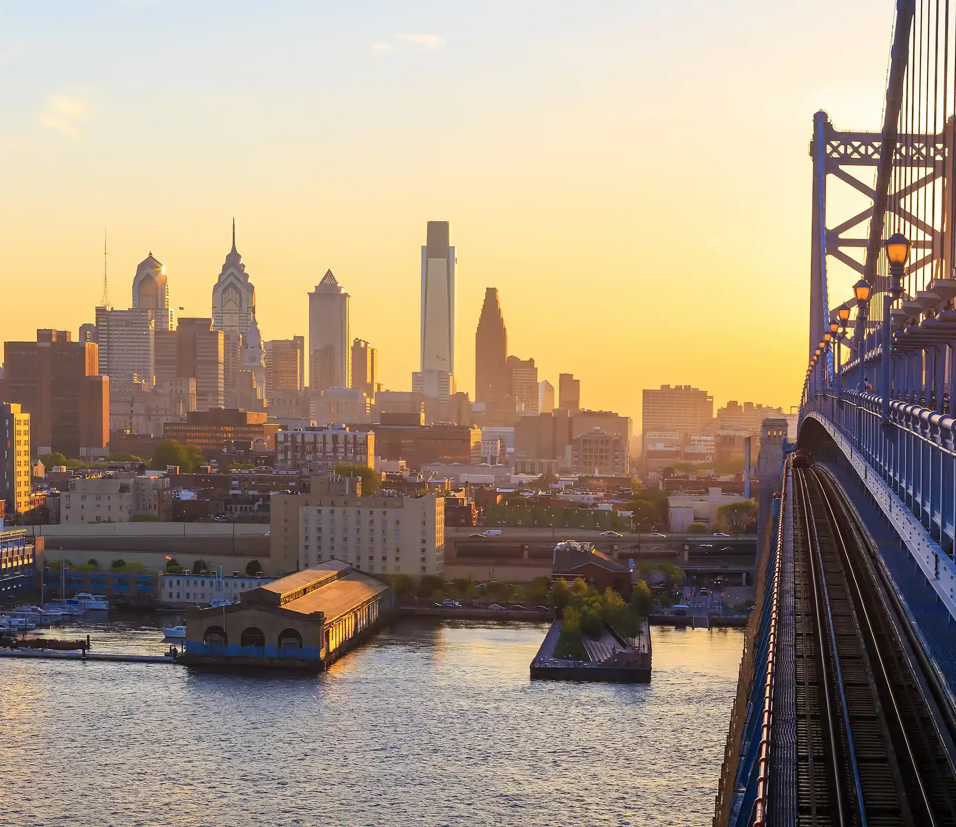 Curving rural road lined with lush cornfields, rolling hills, and distant houses under a bright blue sky.